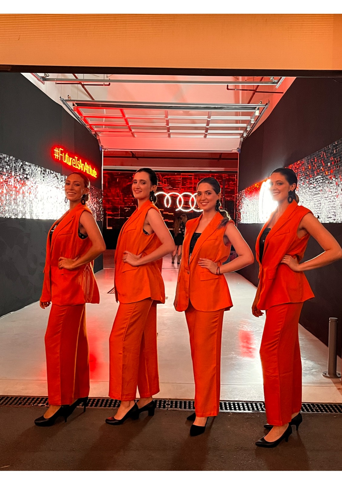 Cuatro promotoras con trajes naranjas en la entrada iluminada de un evento de Audi.