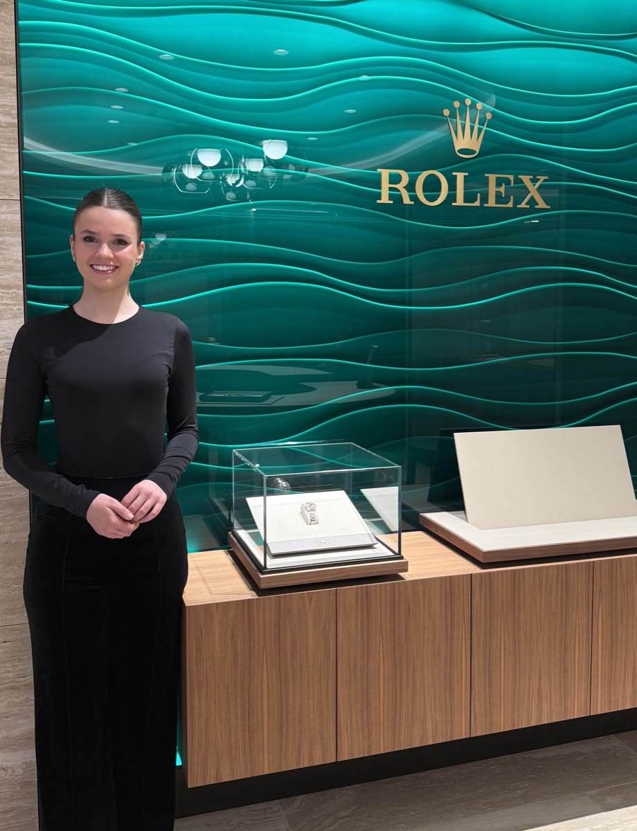 Anfitriona junto a una vitrina de relojes Rolex.
