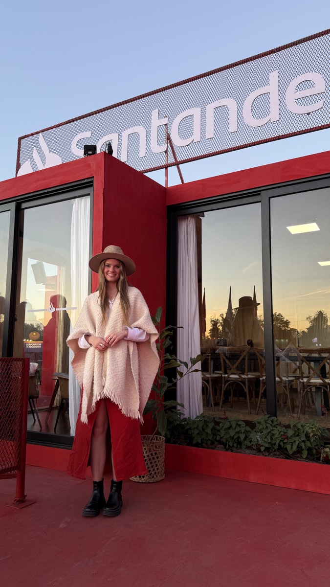 Anfitriona con poncho rosado frente a un módulo rojo de Santander.